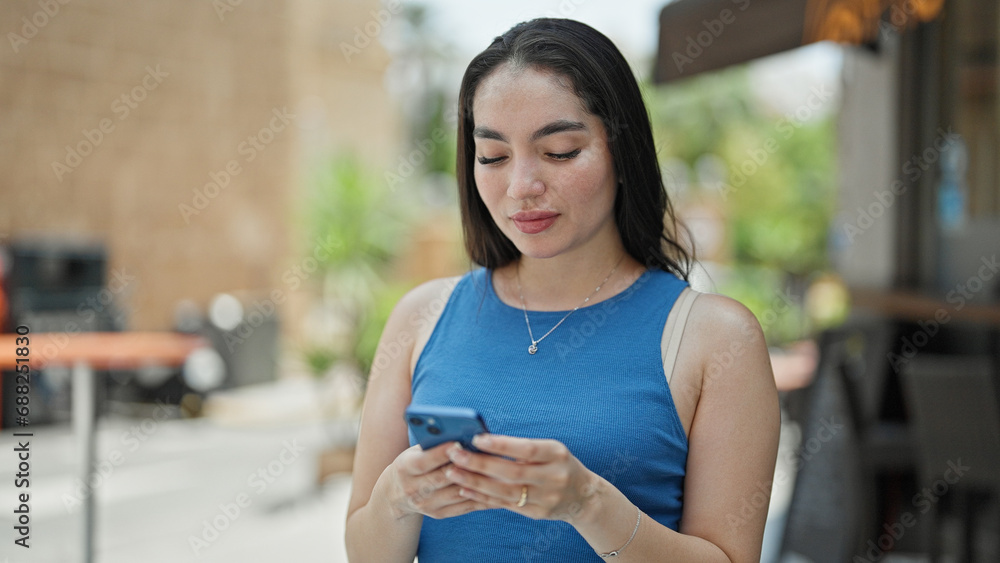 Young beautiful hispanic woman using smartphone with serious expression at coffee shop terrace