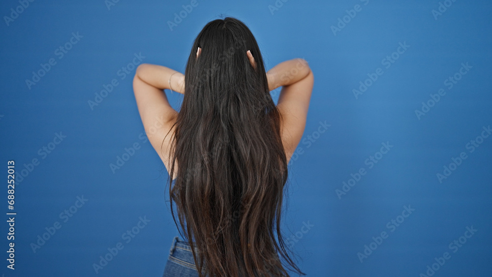 Obraz premium Young beautiful hispanic woman touching her hair backwards over isolated blue background
