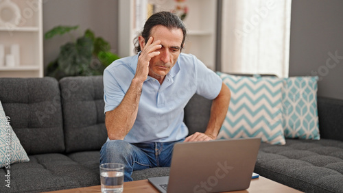 Middle age man using laptop sitting on sofa stressed at home