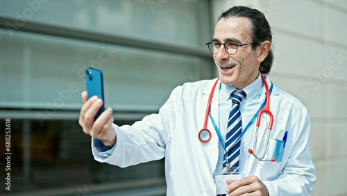 Middle age man doctor doing video call with smartphone smiling at hospital