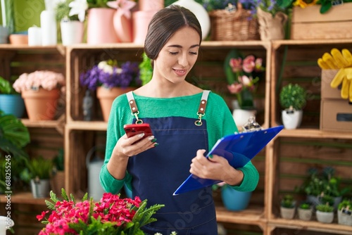 Young beautiful hispanic woman florist using smartphone reading document at flower shop