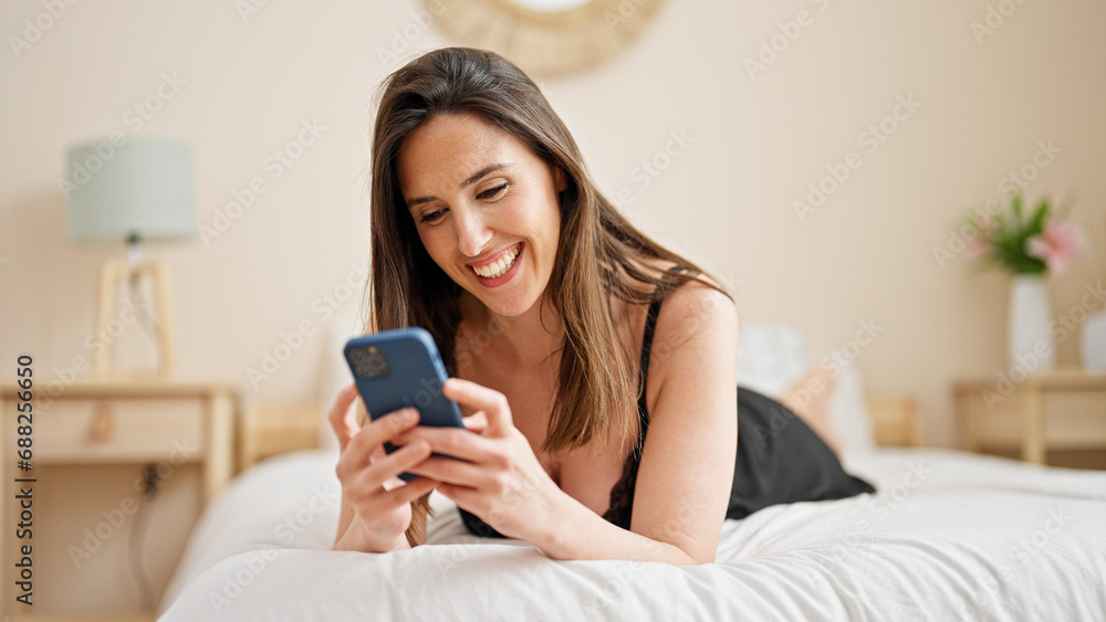 Young beautiful hispanic woman using smartphone lying on bed at bedroom Young beautiful hispanic woman using smartphone lying on bed at bedroom