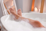 Woman taking bath in tub with foam indoors, closeup