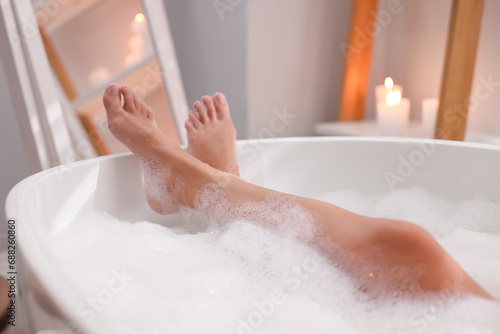 Woman taking bath in tub with foam indoors, closeup photo