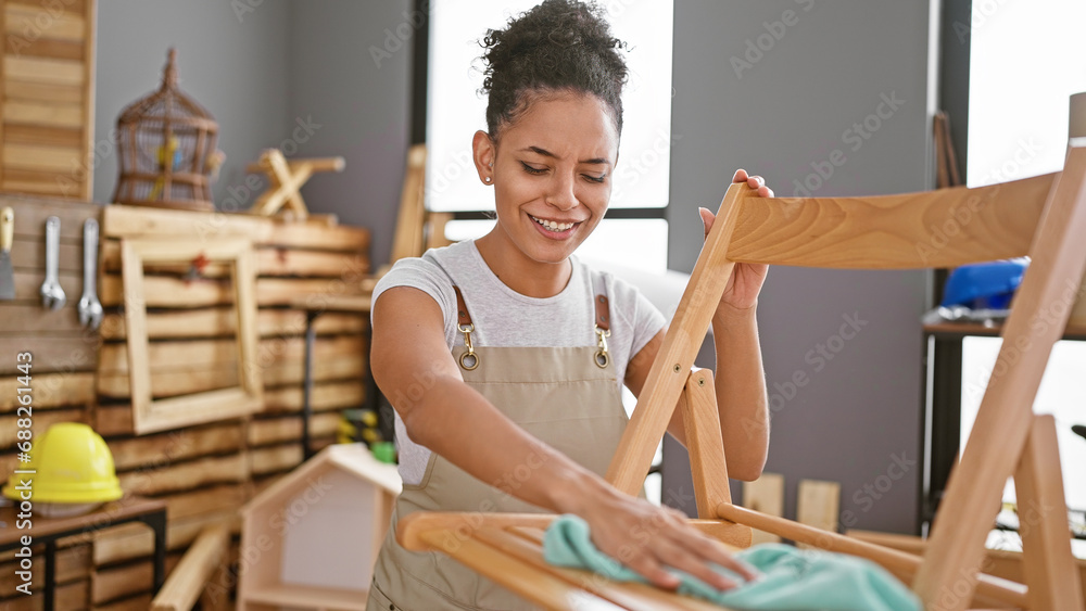 Obraz premium Young beautiful hispanic woman carpenter smiling confident cleaning wood chair at carpentry
