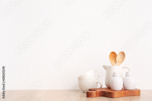 Set of crockery and kitchen utensils on wooden table near white wall