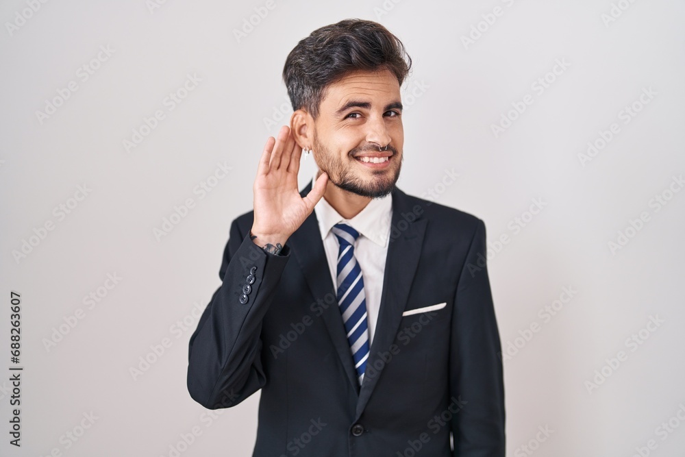 Young hispanic man with tattoos wearing business suit and tie smiling with hand over ear listening an hearing to rumor or gossip. deafness concept. Young hispanic man with tattoos wearing business suit and tie smiling with hand over ear listening an hearing to rumor or gossip. deafness concept.
