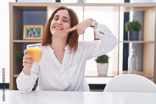 Brunette woman drinking glass of orange juice smiling cheerful showing and pointing with fingers teeth and mouth. dental health concept.