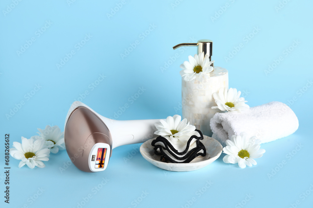 Modern photoepilator with bath supplies and beautiful flowers on blue background Modern photoepilator with bath supplies and beautiful flowers on blue background