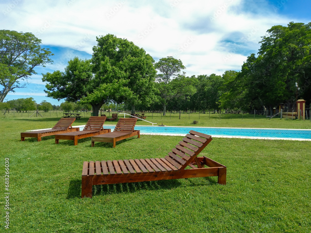 Deckchairs on the lawn beside the swimming pool for relaxation in a tranquil meadow full of trees Deckchairs on the lawn beside the swimming pool for relaxation in a tranquil meadow full of trees