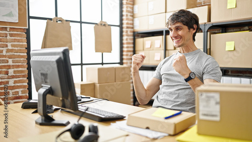 Young hispanic man ecommerce business worker sitting on table with winner gesture at office