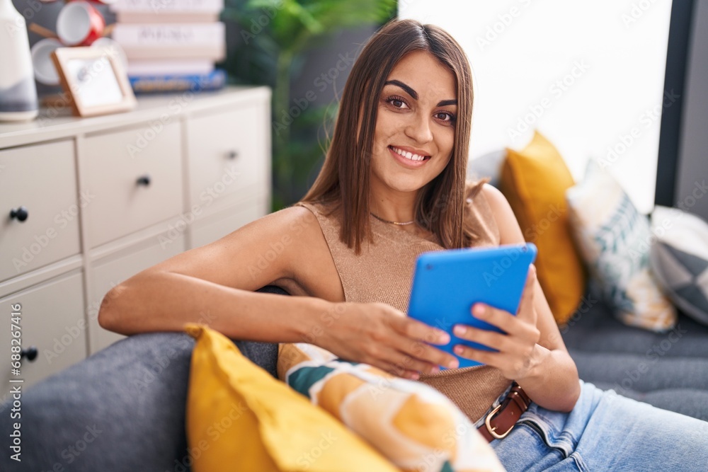 Young beautiful hispanic woman using touchpad sitting on sofa at home Young beautiful hispanic woman using touchpad sitting on sofa at home