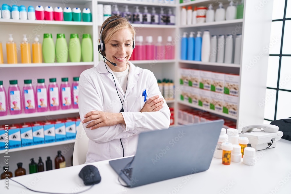 Young caucasian woman working at pharmacy drugstore using laptop happy face smiling with crossed arms looking at the camera. positive person.