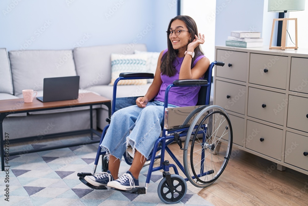 Young hispanic woman sitting on wheelchair at home smiling with hand over ear listening an hearing to rumor or gossip. deafness concept. Young hispanic woman sitting on wheelchair at home smiling with hand over ear listening an hearing to rumor or gossip. deafness concept.