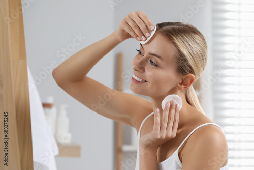 Smiling woman removing makeup with cotton pads in bathroom