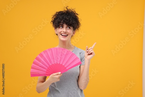 Happy woman holding hand fan on orange background. Space for text photo