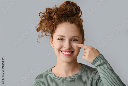 Portrait of pretty young girl pointing at her nose on grey background