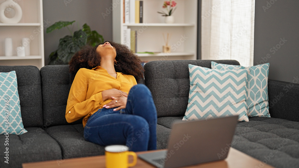 African american woman using laptop suffering for stomach pain at home African american woman using laptop suffering for stomach pain at home