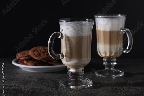 Aromatic latte macchiato in glasses and chocolate cookies on dark grey table
