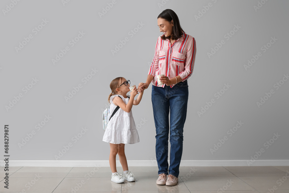 Beautiful mother and her cute little daughter with cups of tea near grey wall Beautiful mother and her cute little daughter with cups of tea near grey wall