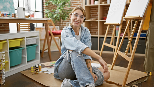 Young woman artist smiling confident sitting on floor at art studio