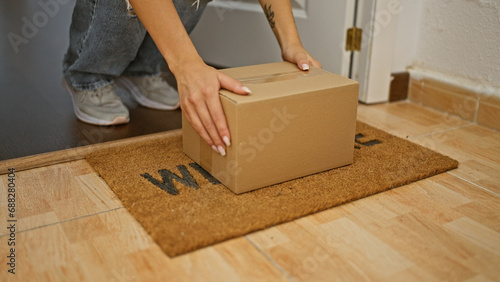 Young woman opening door holding package at home photo