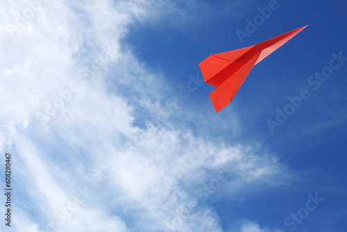 Red paper plane flying in blue sky with clouds