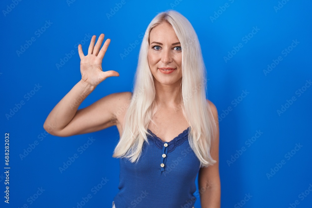 Fototapeta premium Caucasian woman standing over blue background showing and pointing up with fingers number five while smiling confident and happy.