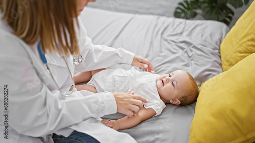 Confident female doctor joyfully examining adorable baby, sitting on bed in cozy bedroom - casual healthcare moment in a loving home environment