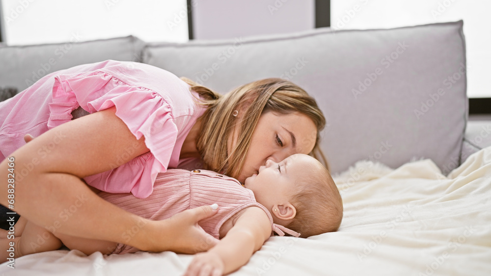 Joyous mother lying on sofa, kissing happy daughter at home in living room, sharing a lovely lifestyle Joyous mother lying on sofa, kissing happy daughter at home in living room, sharing a lovely lifestyle