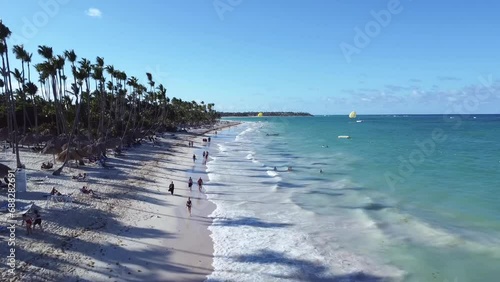 Egzotyczna plaża na której są wczasowicze oraz turkusowy ocean z falami i dużo wysokich palem- ujęcie z drona. photo