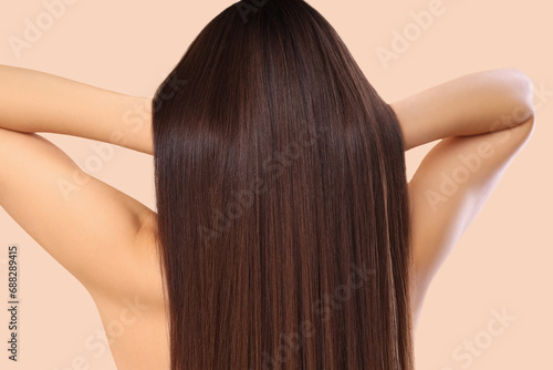 Young brunette woman with beautiful hair on beige background, back view