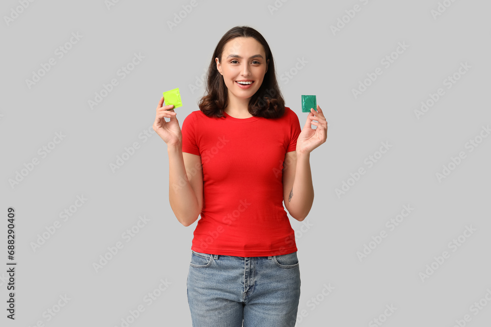 Beautiful young woman with condoms on grey background. Safe sex concept Beautiful young woman with condoms on grey background. Safe sex concept