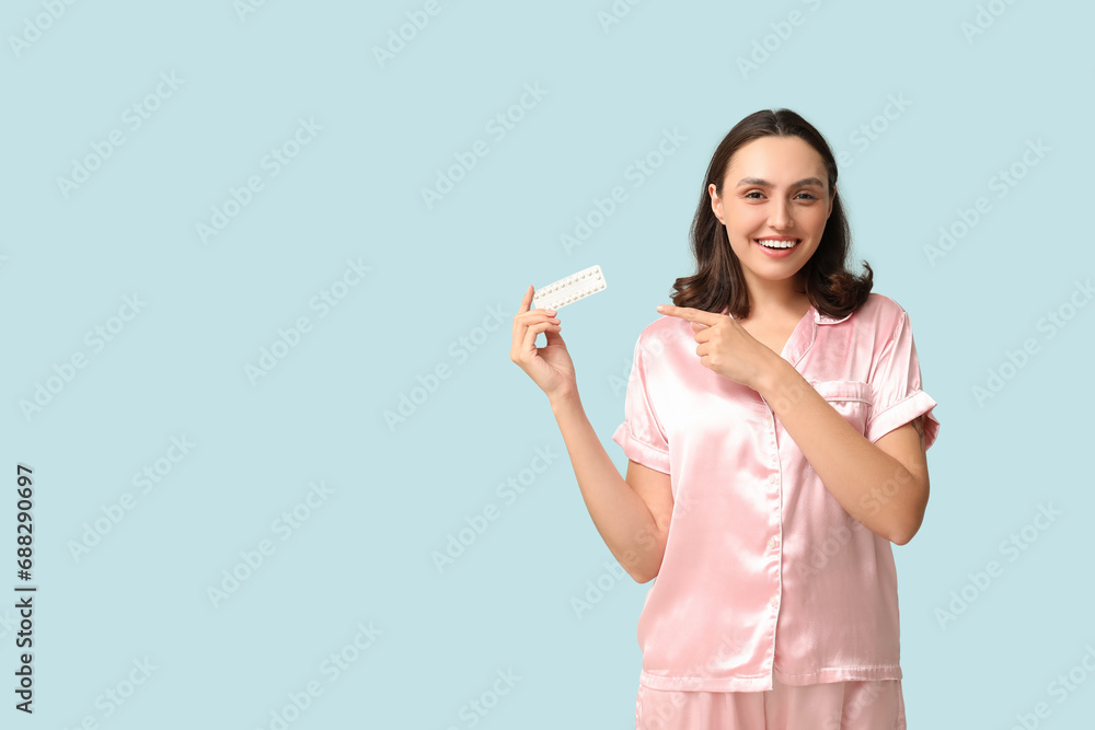 Beautiful young woman pointing at birth control pills on blue background. Safe sex concept Beautiful young woman pointing at birth control pills on blue background. Safe sex concept
