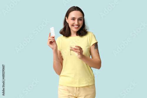 Beautiful young woman with birth control pills and glass of water on blue background. Safe sex concept