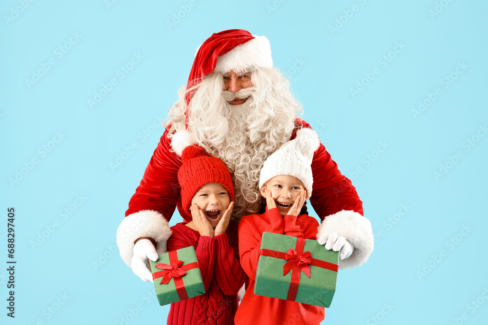 Surprised little children receiving Christmas gifts from Santa Claus on blue background