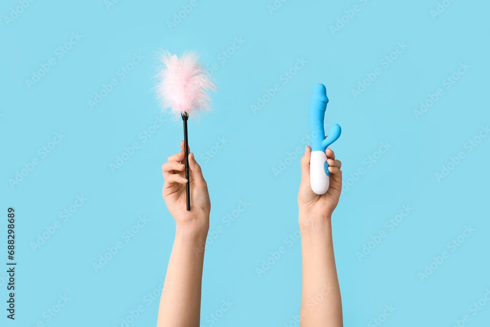 Female hands with vibrator and feather stick from sex shop on color background - obrazy, fototapety, plakaty 