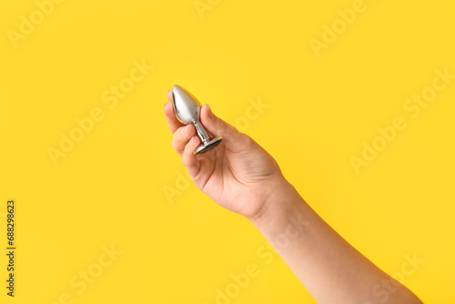 Female hand with anal plug on yellow background, closeup
