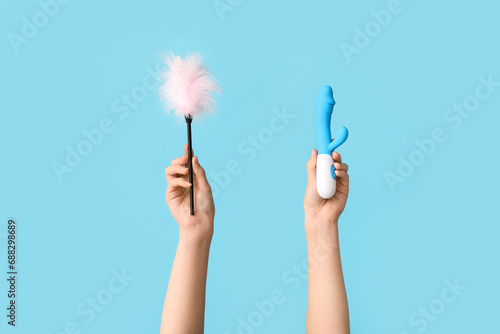 Female hands with vibrator and feather stick from sex shop on color background
