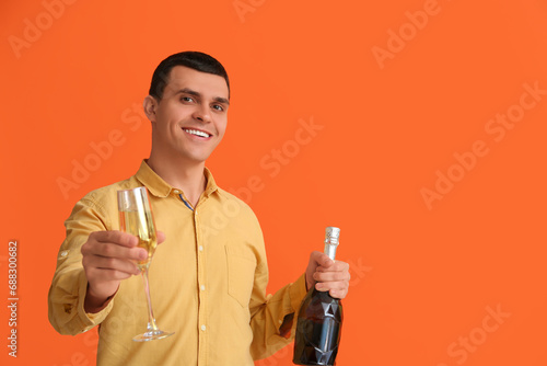 Young man with bottle and glass of champagne celebrating Christmas on orange background