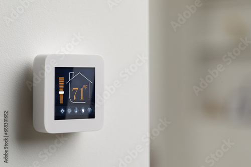 Thermostat displaying temperature in Fahrenheit scale and different icons. Smart home device on white wall, space for text photo