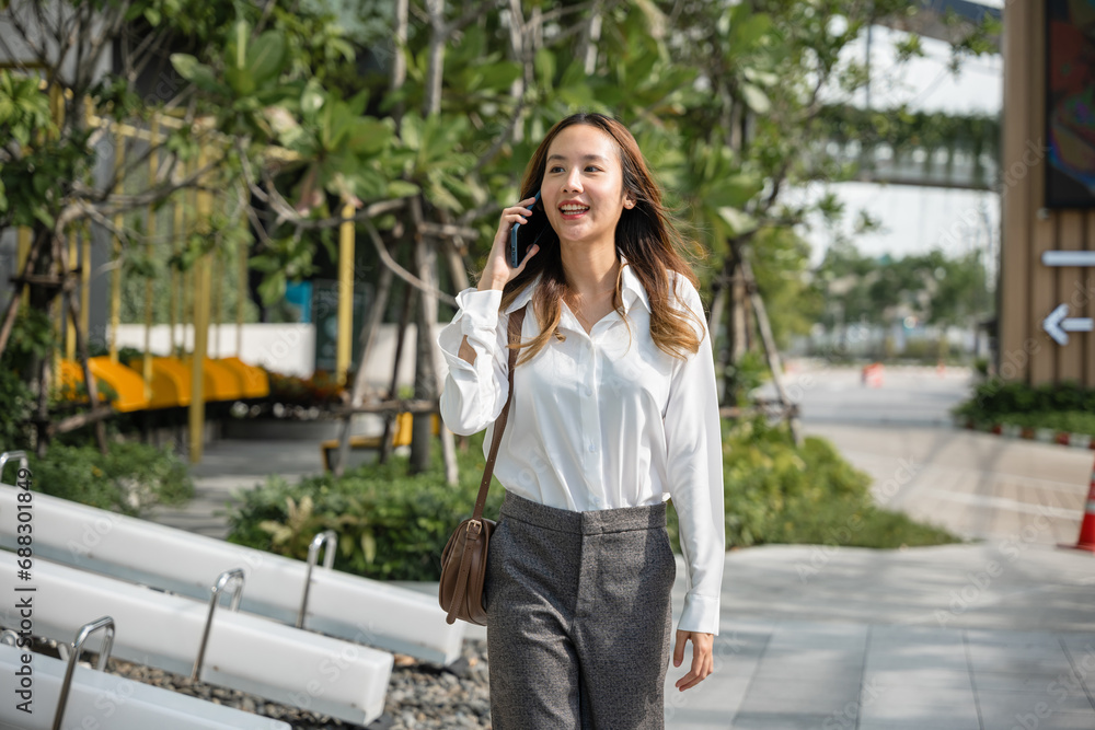 Asian business female calling on smart mobile phone and walking on street outside office building, Happy businesswoman talking on smartphone outdoor in city with client, business communication Asian business female calling on smart mobile phone and walking on street outside office building, Happy businesswoman talking on smartphone outdoor in city with client, business communication