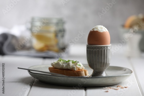 Fresh soft boiled egg in cup and sandwich on white wooden table. Space for text photo