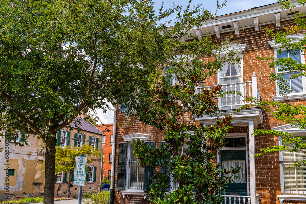 Naklejka premium Charming brick townhouse with green shutters nestled among mature trees in Savannah, Georgia, USA
