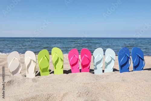 Many stylish colorful flip flops on beach sand