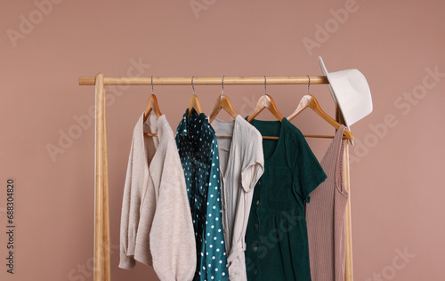 Rack with hat and stylish women`s clothes on wooden hangers against beige background