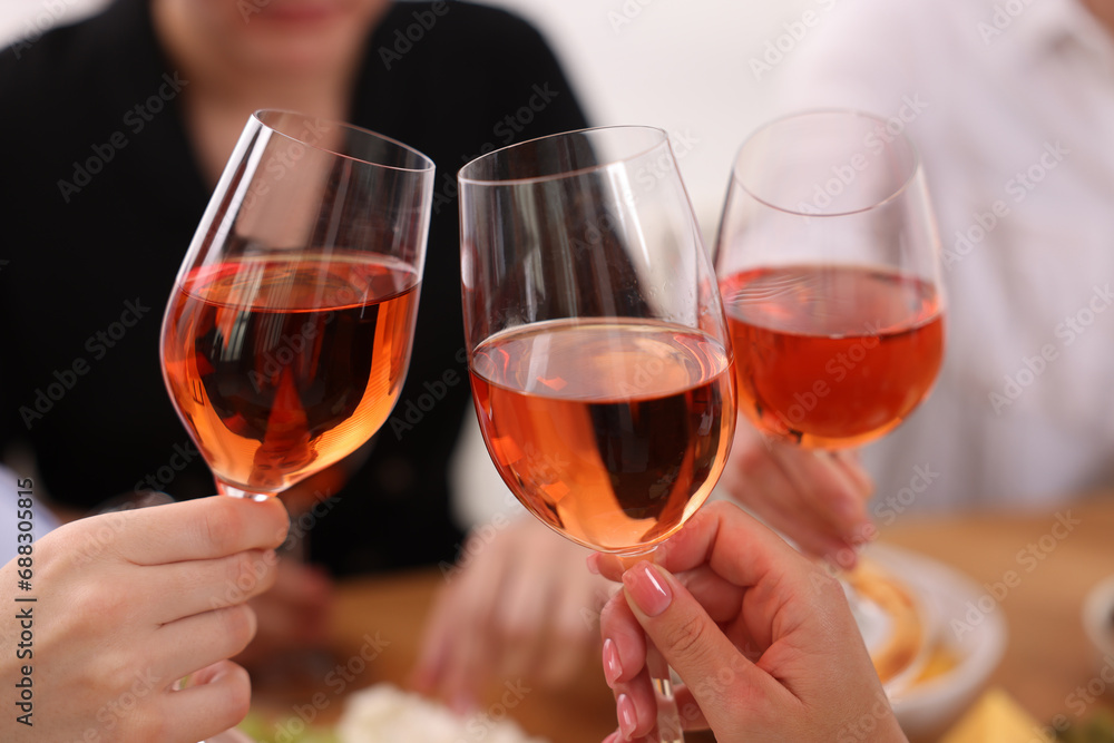 People clinking glasses with rose wine indoors, closeup