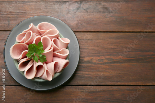 Slices of delicious boiled sausage with parsley on wooden table, top view. Space for text