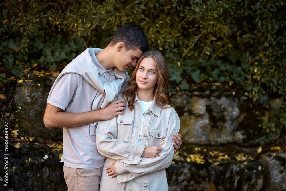 Fototapeta premium Young Cute Female Hugs Boyfriend. In Autumn Outdoor. Lovers Walking in Park. Attractive Funny Couple. Lovestory in Forest. Man and Woman. Cute Lovers in the Park. Family Concept. Happy Couple.