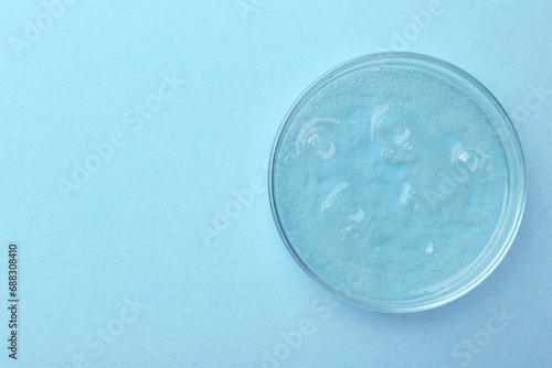 Petri dish with color liquid sample on light blue background, top view. Space for text